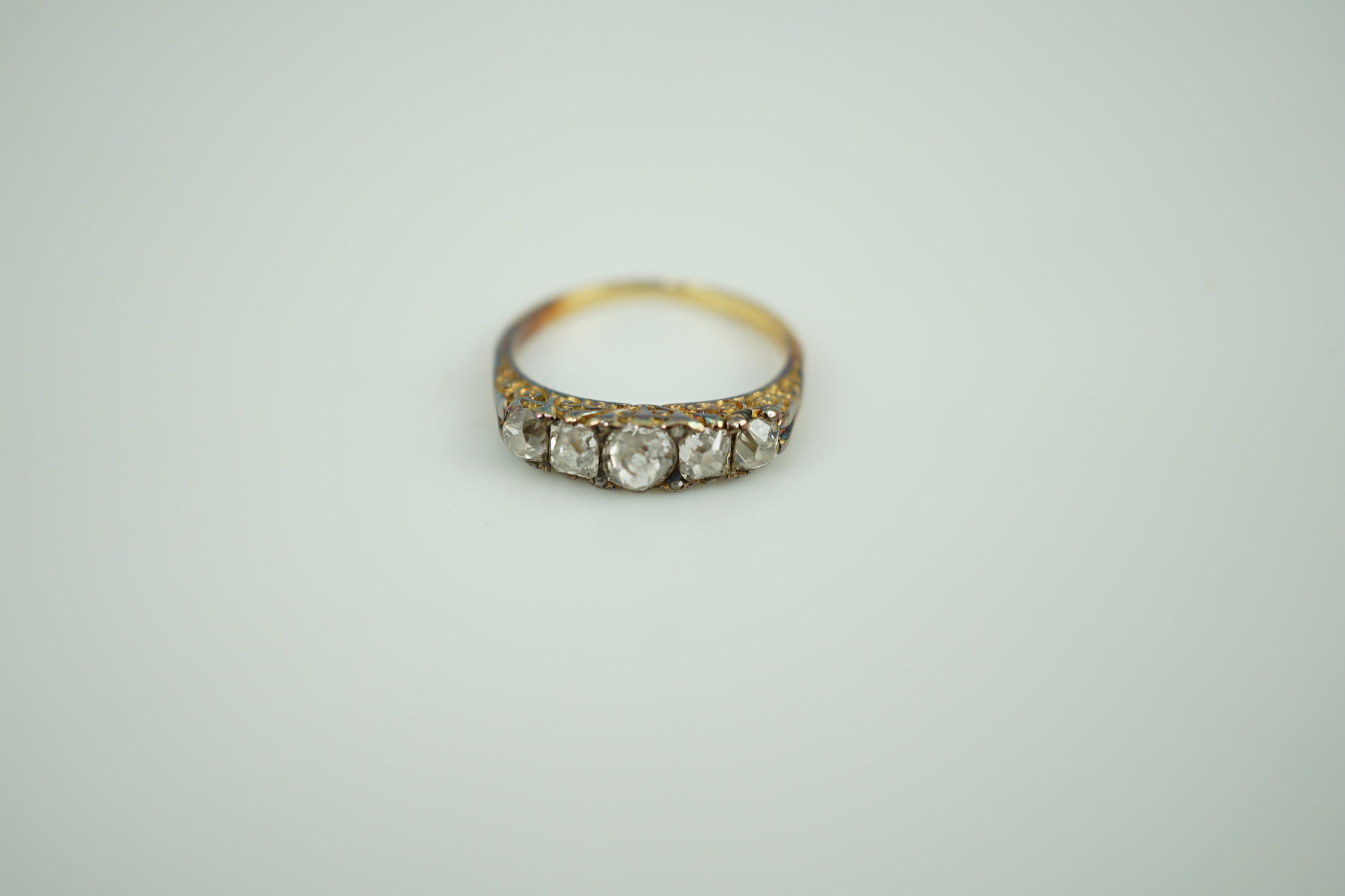 An early 20th century yellow metal and graduated five stone old round cut diamond set half hoop ring, with diamond chip spacers, size K, gross weight 2.8 grams.